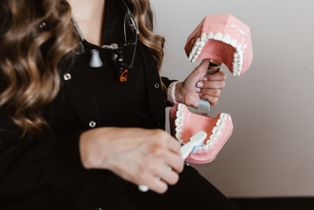 Dental professional holding a large model of teeth and using a toothbrush to demonstrate proper brushing technique—part of patient education during a dental cleaning at Centerpoint Dental.