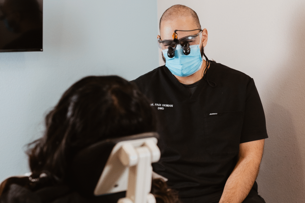 Dr. Fadi Demian, DMD, wearing magnifying loupes and a face mask, sits and attentively consults with a patient during a dental appointment at Centerpoint Dental.